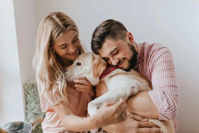 Positive Husband Wife Play With Dog Man Striped Shirt Hugs Labrador With Tenderness